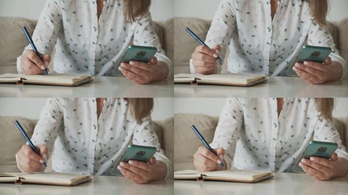 女人的手使用手机并在笔记本上书写