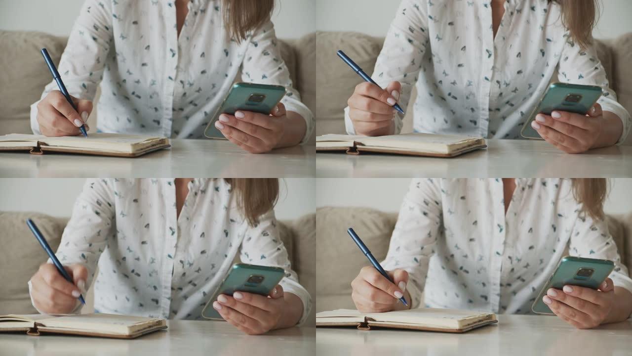 女人的手使用手机并在笔记本上书写