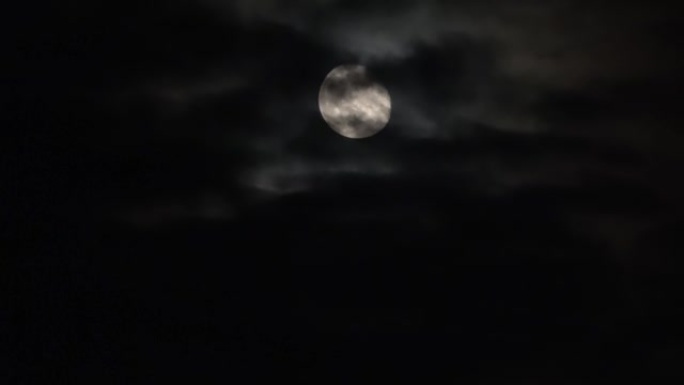 晚上在明亮的月亮上看，有一些云经过。