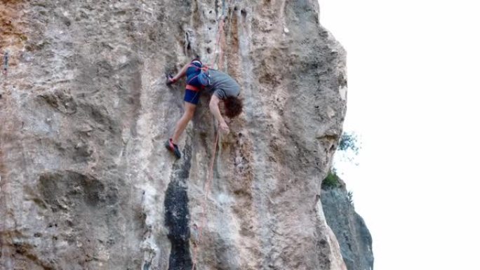 强壮而熟练的男子登山者通过具有挑战性的路线爬上垂直的石灰墙岩壁，登山者处于膝盖位置，双手休息良好，握