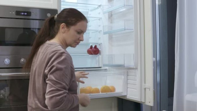女人把食物放在冰箱里，干净的集成冰箱内置厨房外壳。当代公寓室内，新的现代白色厨房。