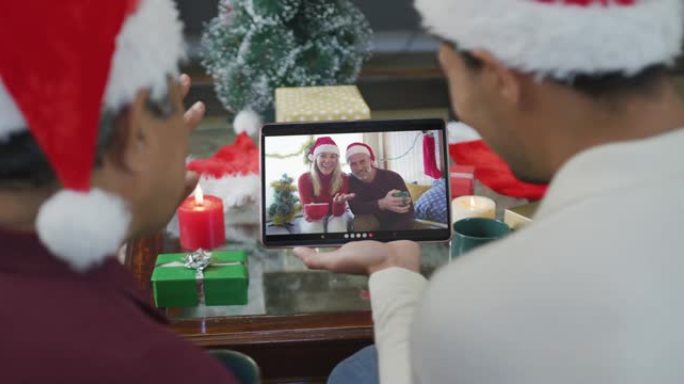 带有圣诞老人帽子的混血儿父子使用平板电脑进行圣诞节视频通话，屏幕上有情侣