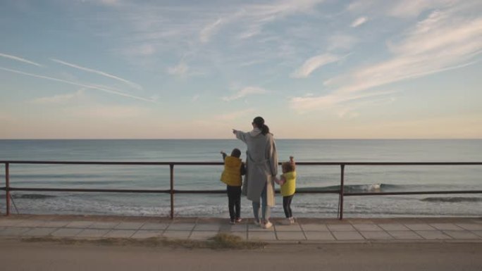 母亲和两个孩子从人行道上看海时的背景图