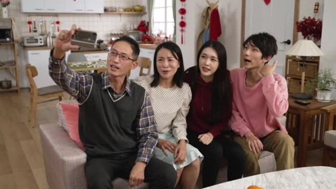 在农历新年假期期间，亚洲家庭在家里通过智能手机上的视频聊天与朋友进行现场交谈时，挥舞着手并试图获得消