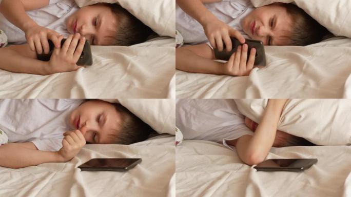 早上7-9岁的高加索男孩在床上关闭智能手机上的闹钟，用枕头遮住耳朵，继续睡觉。这个男生不想醒来上学。