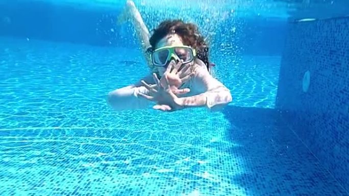 女孩戴着面具在游泳池水下游泳。