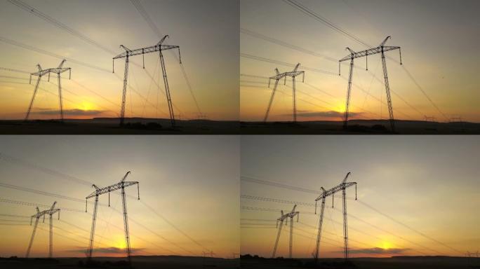 日出时带有电力线的高压塔的深色轮廓。