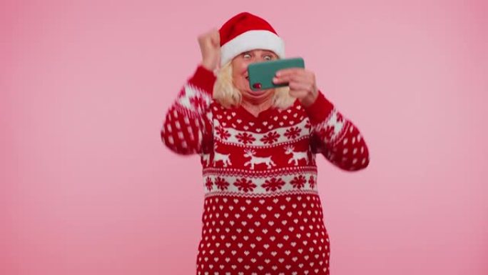 穿着圣诞毛衣的忧心忡忡的奶奶热情地在手机上玩赛车视频游戏