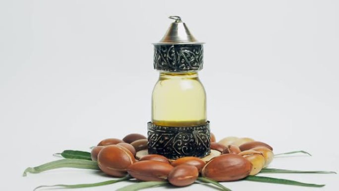东方玻璃和金属瓶中的摩洛哥坚果油和白色背景上绿叶运动的摩洛哥坚果油