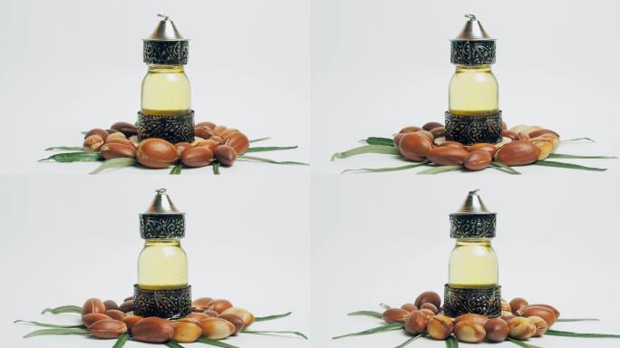 东方玻璃和金属瓶中的摩洛哥坚果油和白色背景上绿叶运动的摩洛哥坚果油