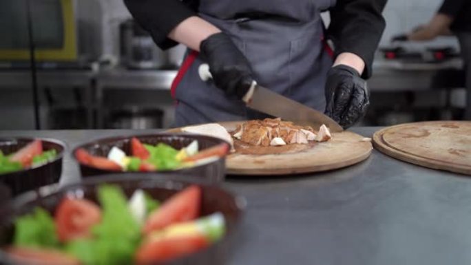 餐厅送餐。女厨师的手特写切煮鸡肉做沙拉。一次性塑料盒。