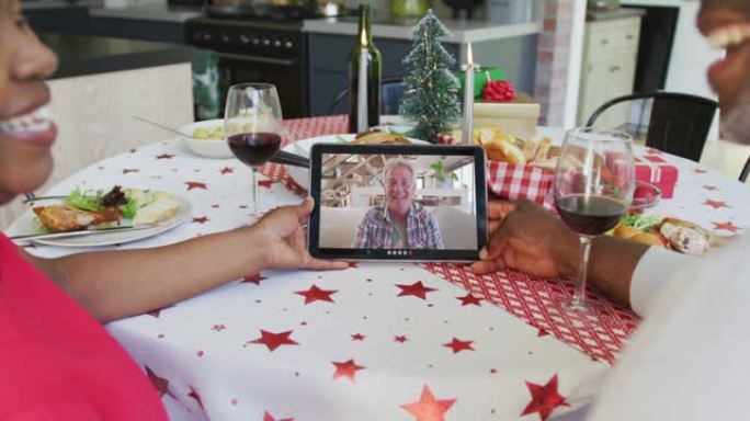 微笑的非洲裔美国夫妇使用平板电脑与屏幕上的快乐男人进行圣诞节视频通话