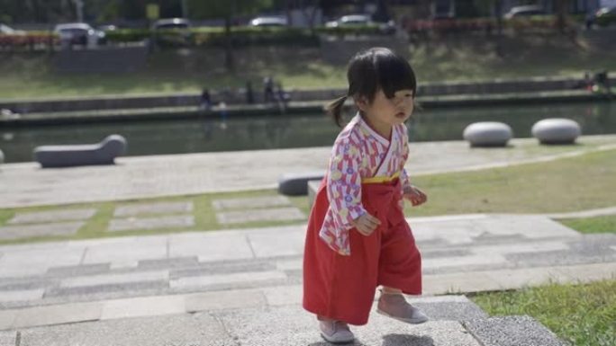 穿着传统服装的可爱的日本蹒跚学步的孩子在阳光明媚的日子里在公园外面玩耍时蹒跚着上楼梯。