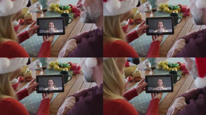 白人夫妇戴着圣诞老人帽子，使用平板电脑与屏幕上的女人进行圣诞节视频通话