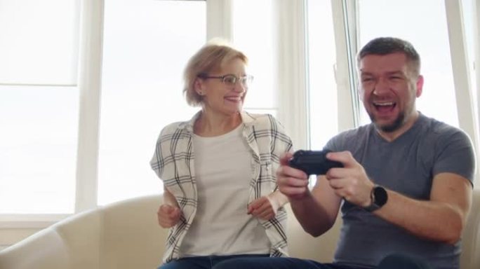幸福的夫妻坐在沙发上玩电子游戏，在恋爱中使用控制器一起玩在线电子游戏