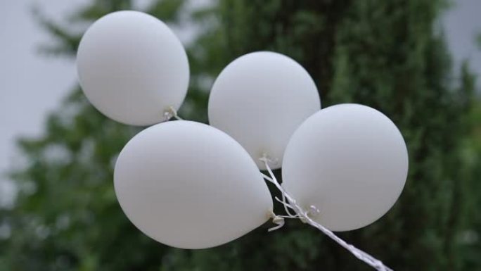 将白色气球绑在户外，公园背景为绿树。派对装饰品以慢动作飞行