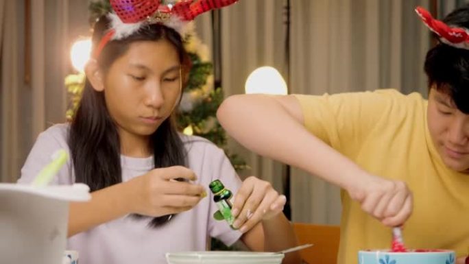 亚洲儿童在晚上在家中将糖中的颜色混合在一起装饰圣诞节饼干。