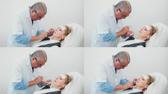 整形外科医生做两次填充注射透明质酸在鼻唇沟妇女病人的脸躺在椅子上。患者注射后感到疼痛