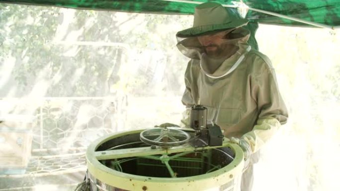 小型企业和有机食品生产概念。一名男性养蜂人将装有蜂蜜的框架放在提取器中。养蜂治疗产品