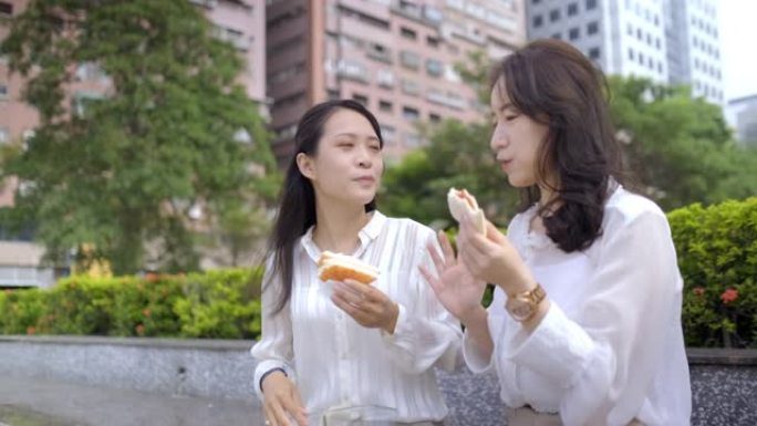 两名亚洲女商人在公园的长凳上吃盒装午餐