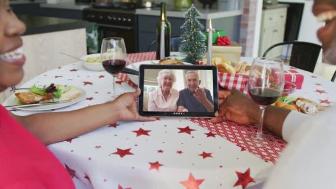 微笑的非洲裔美国夫妇使用平板电脑与屏幕上的幸福夫妇进行圣诞节视频通话