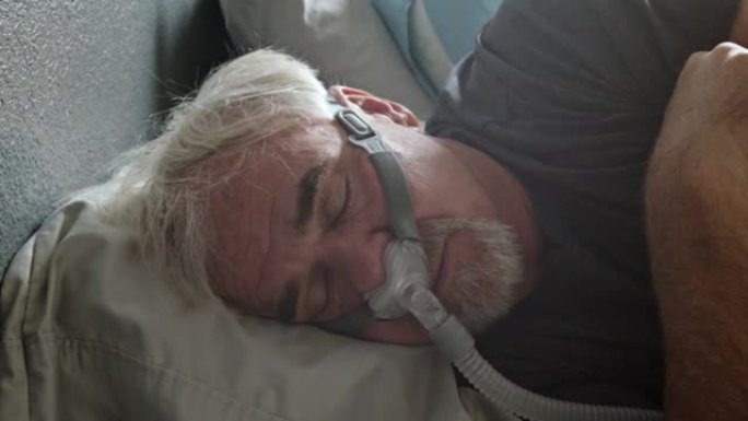 睡眠呼吸暂停的成熟男子在床上睡觉时戴着CPAP面罩