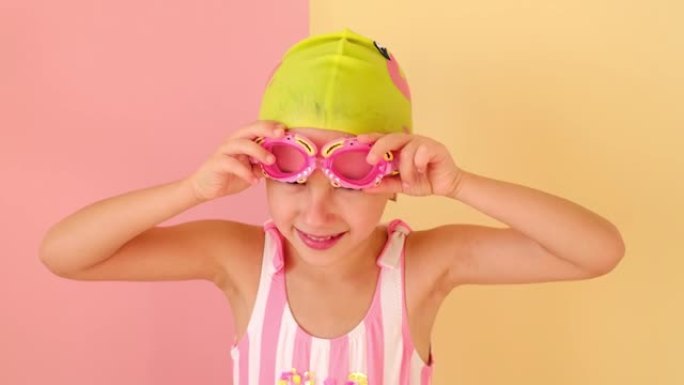 一个戴着游泳帽和条纹粉红色泳衣的女孩戴着螃蟹形状的有趣的儿童泳镜。