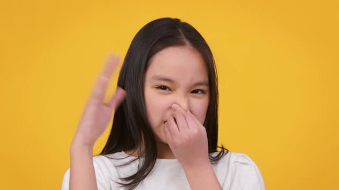 难闻的气味。青春期前的亚洲女孩捂住鼻子，挥舞着手，试图扔掉空气中的臭味