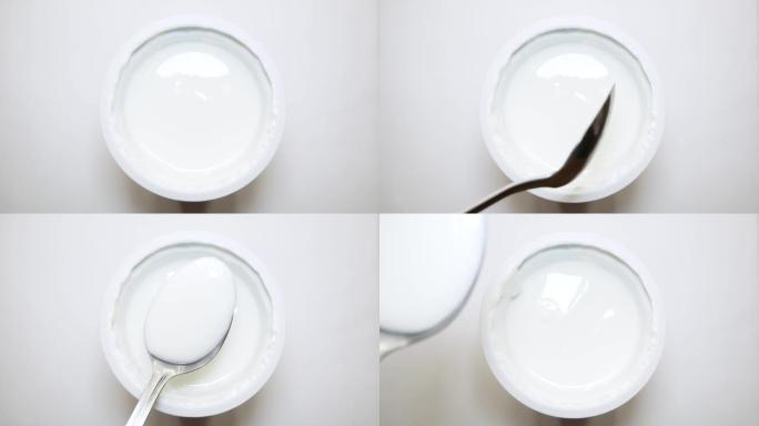 从罐子顶部看，酸奶隔离在白色背景上。吃酸奶勺子特写。4K