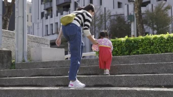 一个现代住宅建筑背景下的公园里，穿着女性传统服饰的日本幼儿在母亲的搀扶下爬上了楼