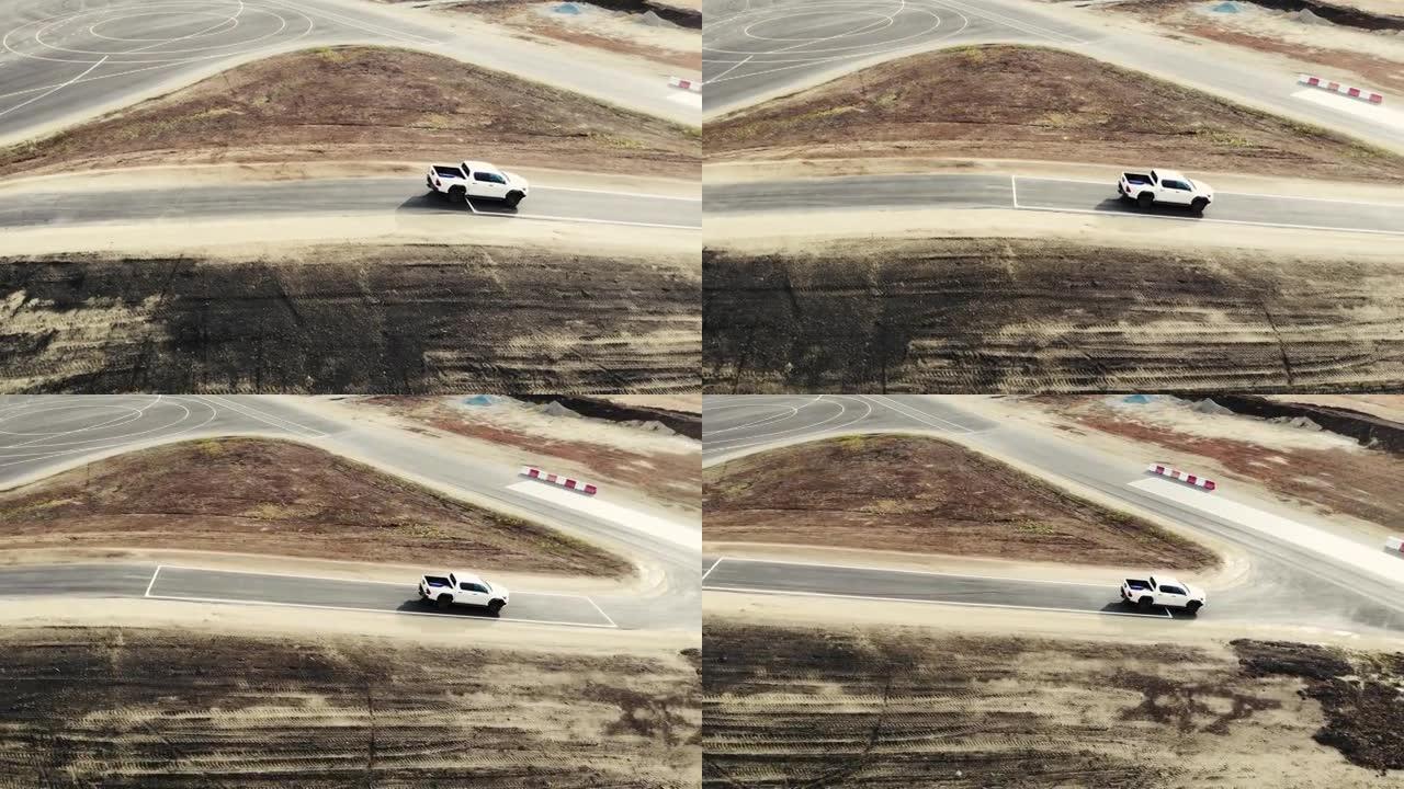 白色皮卡车在试验场下山时的鸟瞰图。汽车的驾驶员检查新路的质量。带有道路标记的黑色沥青。道路建设、试验