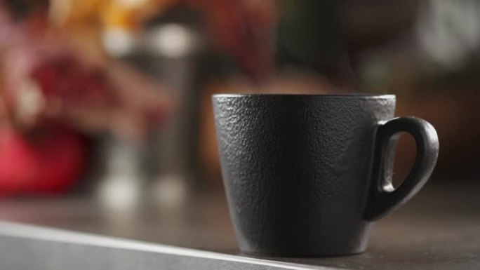 特写热气腾腾的浓缩咖啡或一杯茶，实时视频，选择性聚焦在杯子上。桌子上有蒸汽的热陶瓷黑咖啡杯。早餐的热