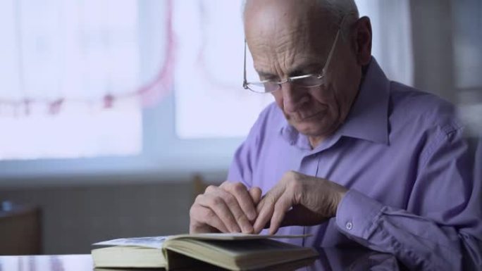 一位戴眼镜的70岁老人坐在木桌旁看书