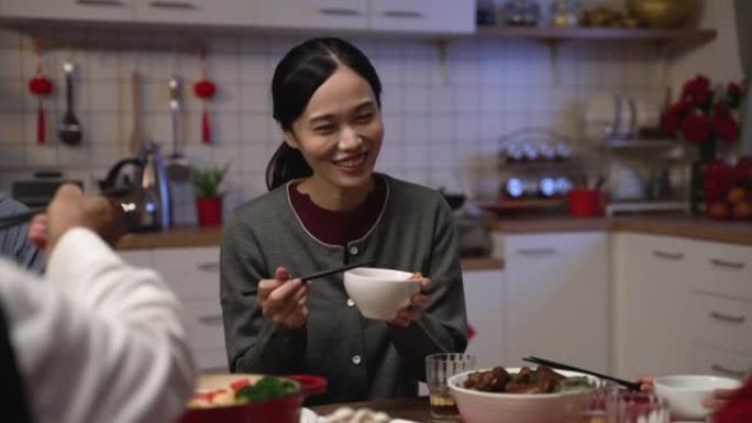 在春节前夕，有选择性的焦点微笑的亚洲daughter妇在餐桌上的碗里从她的老母亲那里接受食物