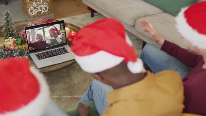 拥有圣诞老人帽子的多元化家庭使用笔记本电脑进行圣诞节视频通话，屏幕上有幸福的家庭