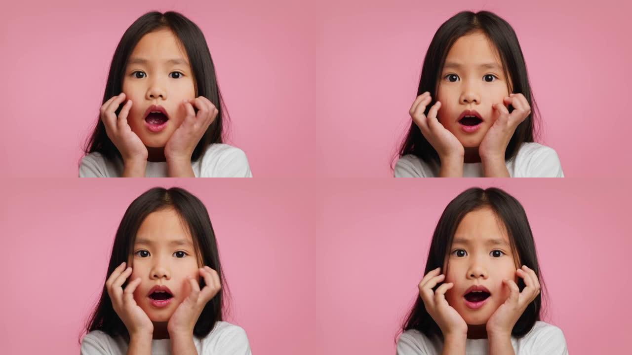 惊讶的韩国小女孩触摸脸在休克，粉红色背景