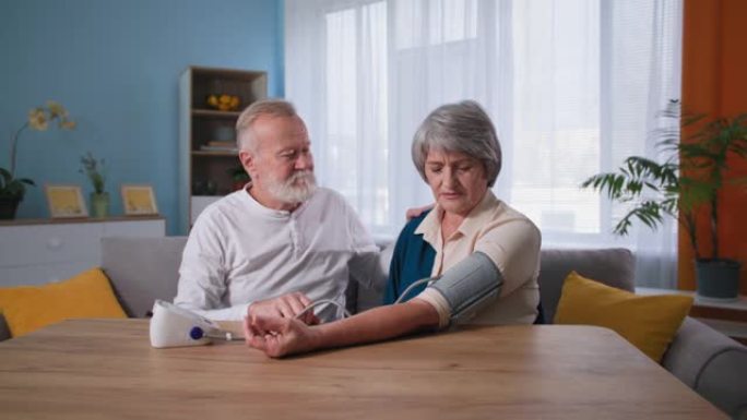 有爱心的老人在餐桌上使用眼压计检查患有高血压的妻子的血压，老夫妇在家照顾健康