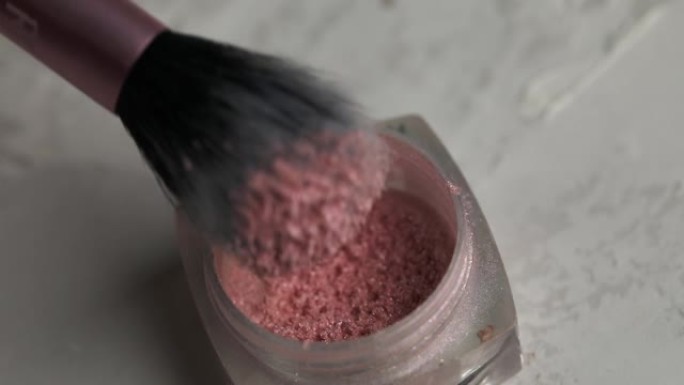 女化妆师拿着一个粉红色亮片的容器，将它们收集在蓬松的刷子上，闪闪发光的眼影纹理，特写镜头。美容概念