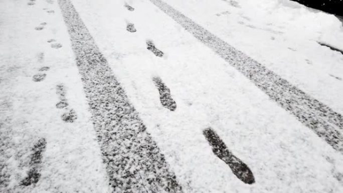 道路上新鲜积雪上的脚印和轮胎痕迹。雪花飘落