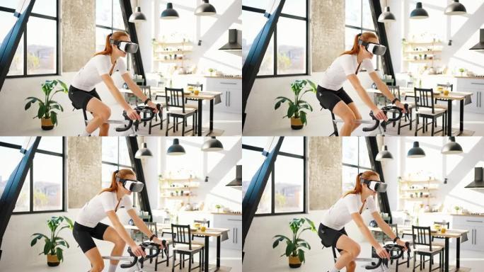 VR耳机中的年轻女性正在踩踏室内自行车教练，微笑着说话。工作室公寓，厨房。在家进行日常训练