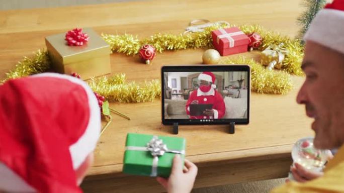 带有圣诞老人帽子的高加索父子使用平板电脑进行圣诞视频通话屏幕上的圣诞老人