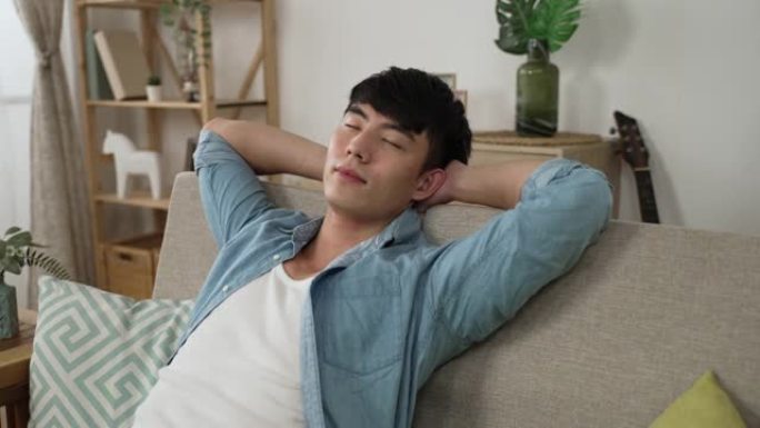 午睡时间在家的客厅里，一个放松的亚洲男性躺在沙发上，双手放在脑后睡个好觉的半身镜头