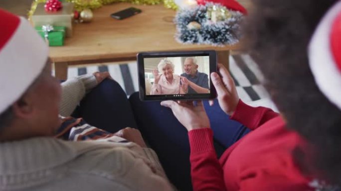 非裔美国母亲和女儿使用平板电脑进行圣诞节视频通话，屏幕上有情侣