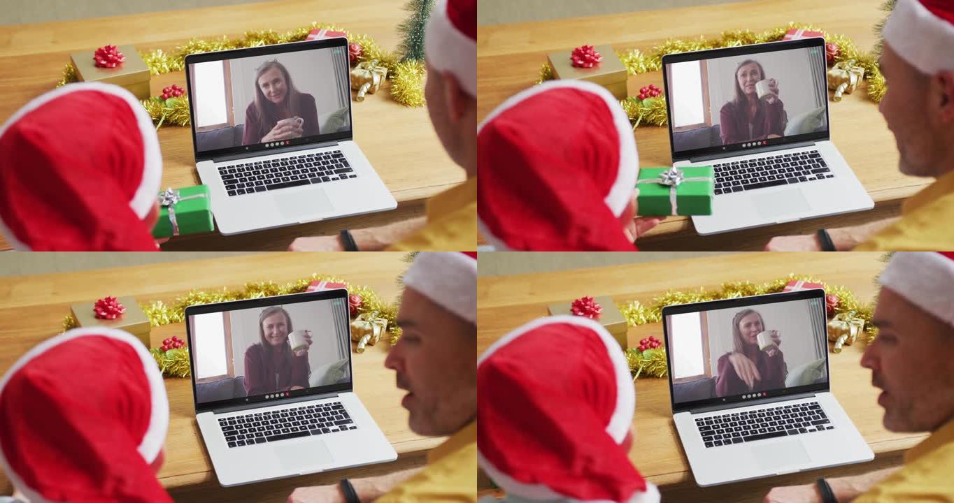 白人父亲和儿子戴着圣诞老人的帽子，使用笔记本电脑与屏幕上的女人进行圣诞节视频通话