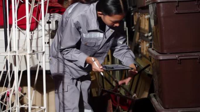 穿着灰色制服的亚洲20多岁妇女在仓库储藏室检查计数物品。维修服务