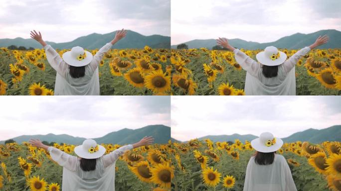 自由的概念，一个奇妙的女人在黄色向日葵地里举起双手的背影。每天都是一个快乐的地方。向日葵田里的夕阳。