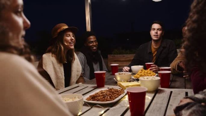 各种各样的成人朋友在晚上的餐桌上在户外聚会上聊天和笑