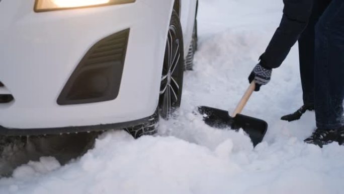 男子从卡住的汽车车轮上挖雪