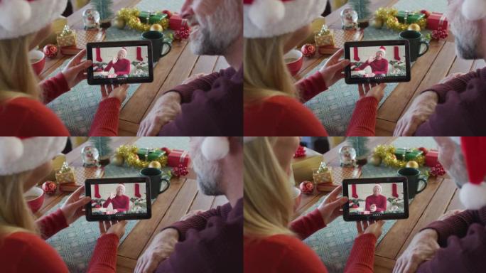 微笑的高加索夫妇戴着圣诞老人的帽子，使用平板电脑与屏幕上的男人进行圣诞节视频通话