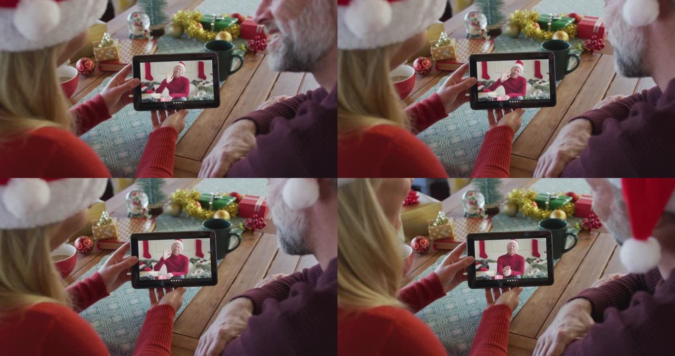 微笑的高加索夫妇戴着圣诞老人的帽子，使用平板电脑与屏幕上的男人进行圣诞节视频通话